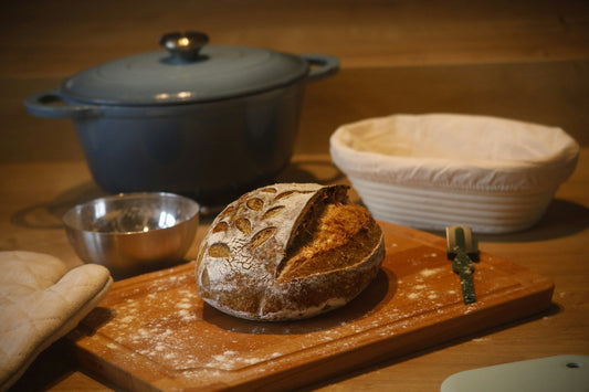 Sourdough bread loaf with banneton basket, Dutch oven, bread lame and baking tools on wooden kitchen counter
