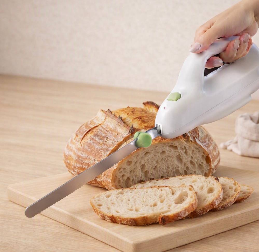 Electric knife slicing sourdough bread on a wooden cutting board
